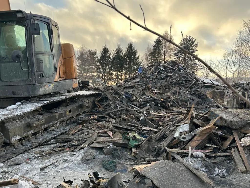 Une grande excavatrice se tient devant un tas de gravats.