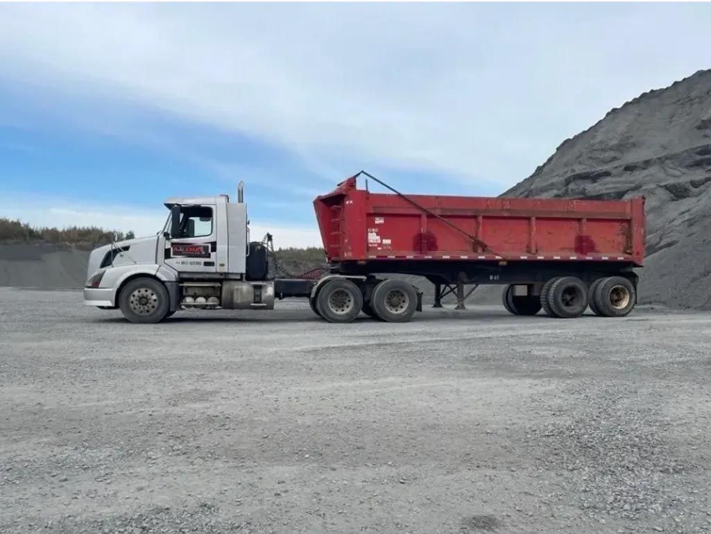 Un camion à benne basculante blanc avec une remorque rouge est garé sur un terrain en gravier.