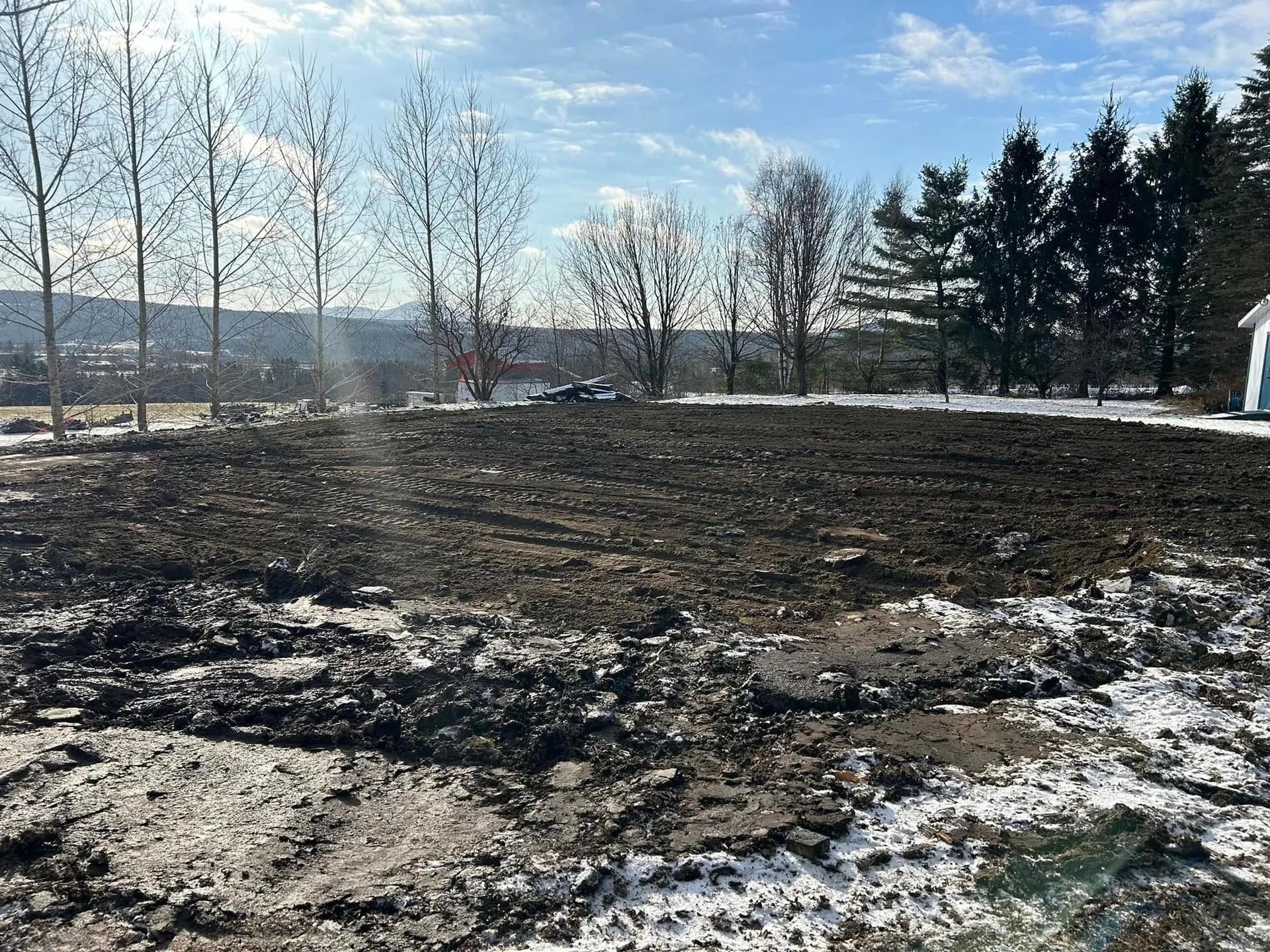 Un champ boueux avec des arbres en arrière-plan et une maison au loin.