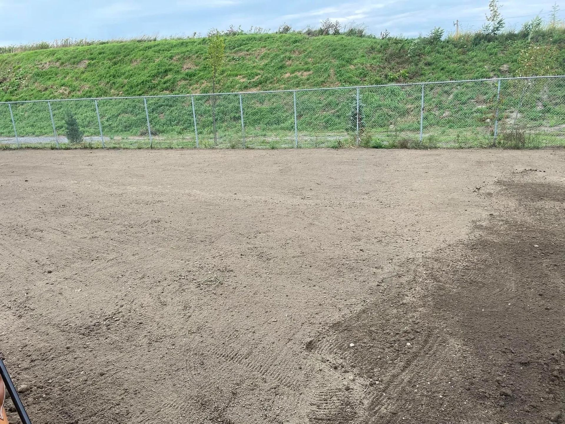 Une personne se tient dans un champ de terre avec une clôture en arrière-plan.