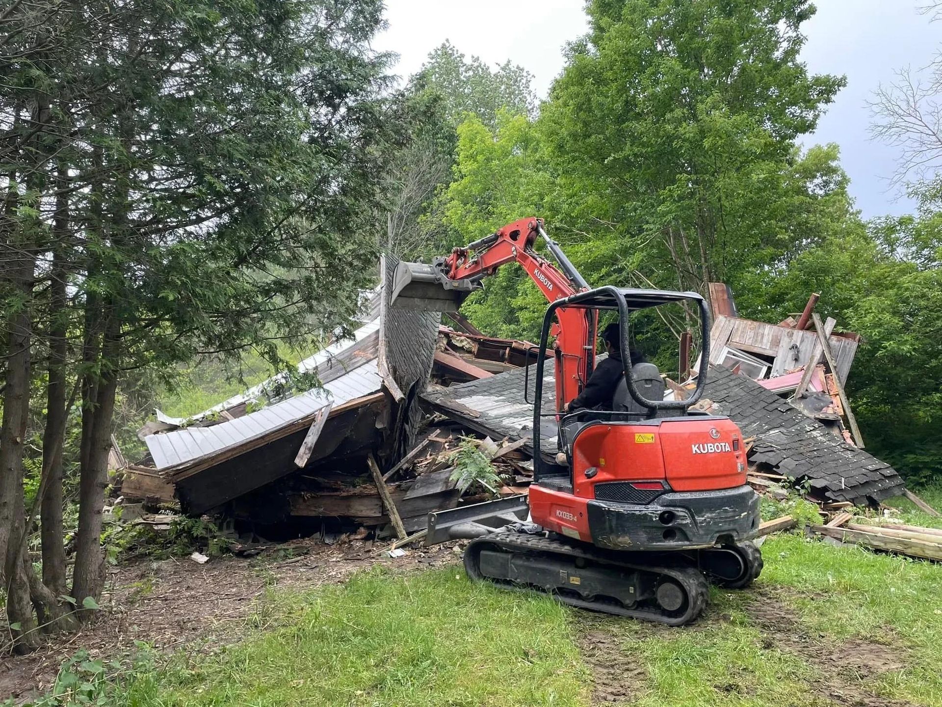 Une petite excavatrice rouge démolit un bâtiment dans un champ.