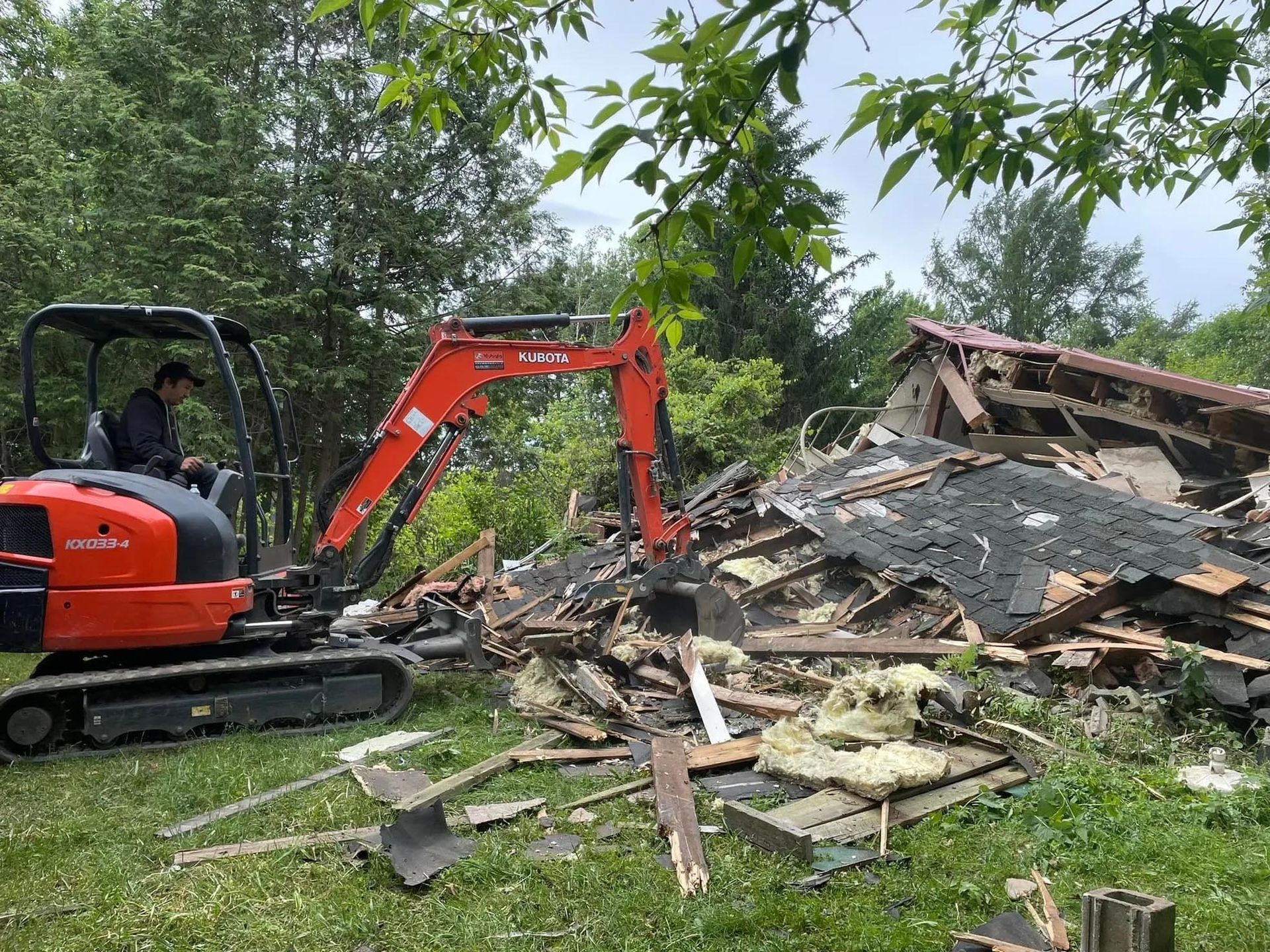 Un homme conduit une excavatrice à côté d'un tas de bois.