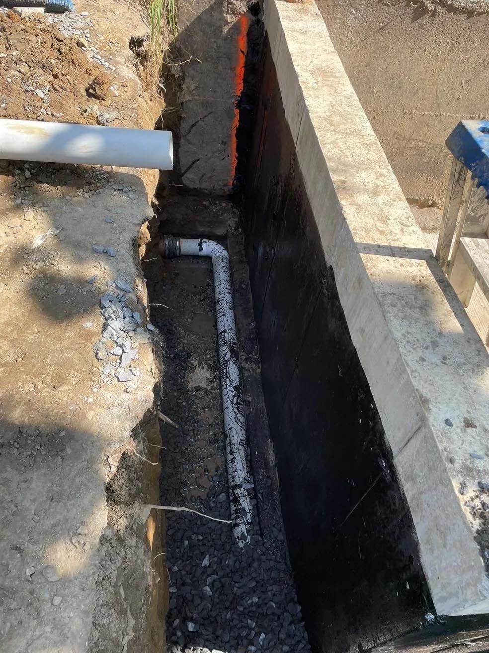 Un tuyau est en cours d'installation dans une tranchée à côté d'un mur.