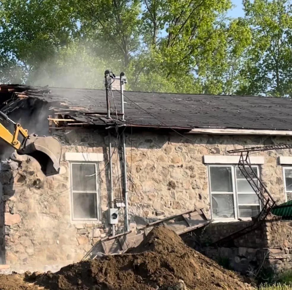 Un grand bâtiment en pierre est en train d'être démoli par un bulldozer.