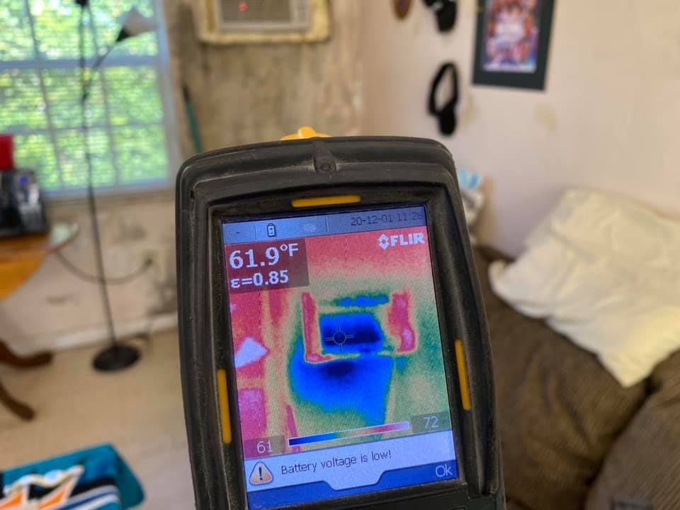 Thermal camera shows cold spot on a wall. The device displays a reading of 61.9 degrees Fahrenheit.
