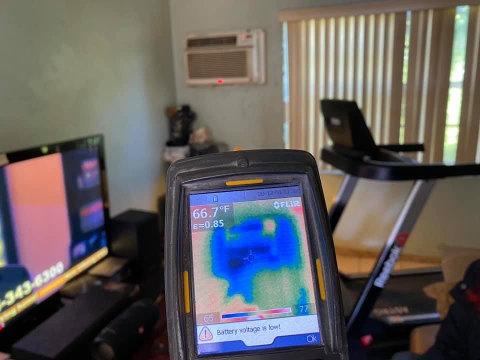Thermal camera showing a blue air conditioner against a green wall, indoors.