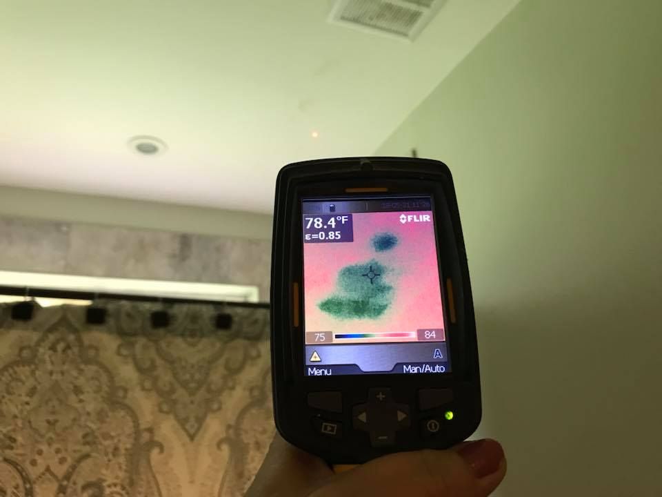 Hand holding thermal camera pointed at ceiling, showing cool spot indicated in green.
