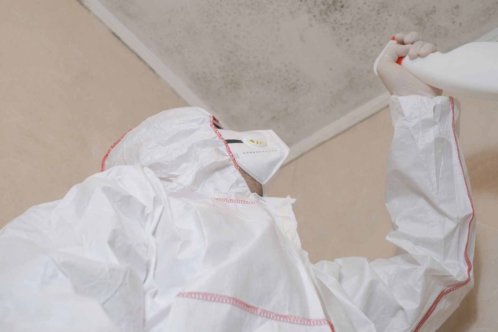 Person in protective suit inspecting ceiling with mold.