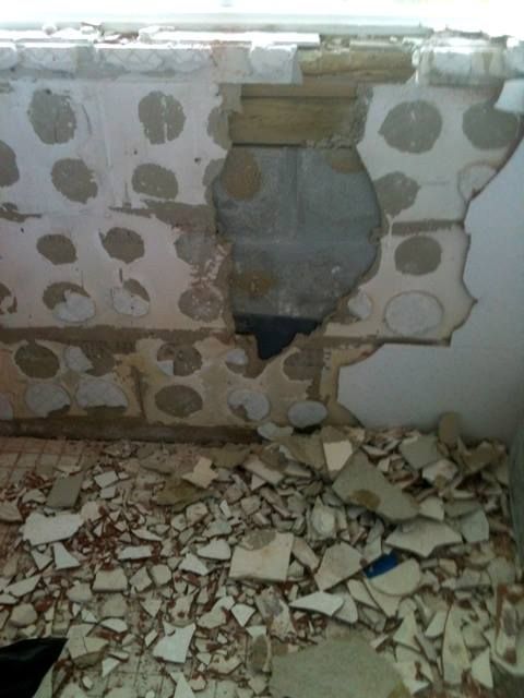 Demolished interior; ceiling and floor tiles broken, debris scattered. Grey, white, brown colors.