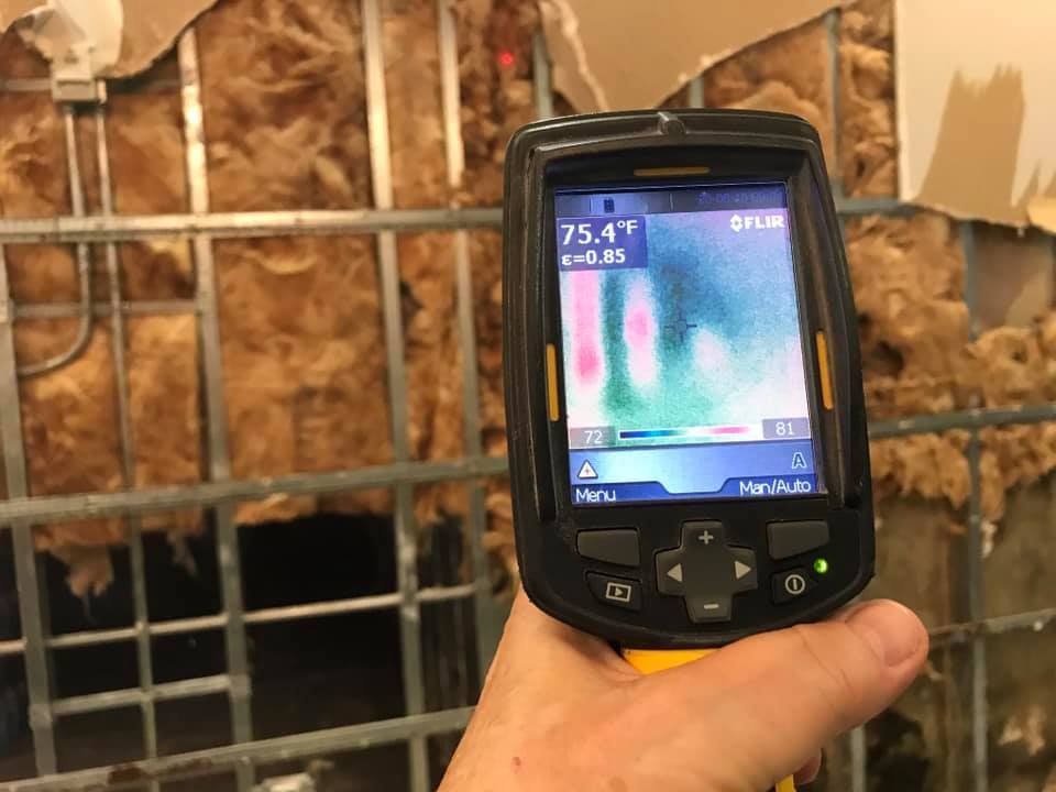 Hand holding thermal camera pointed at a wall with exposed insulation and metal 