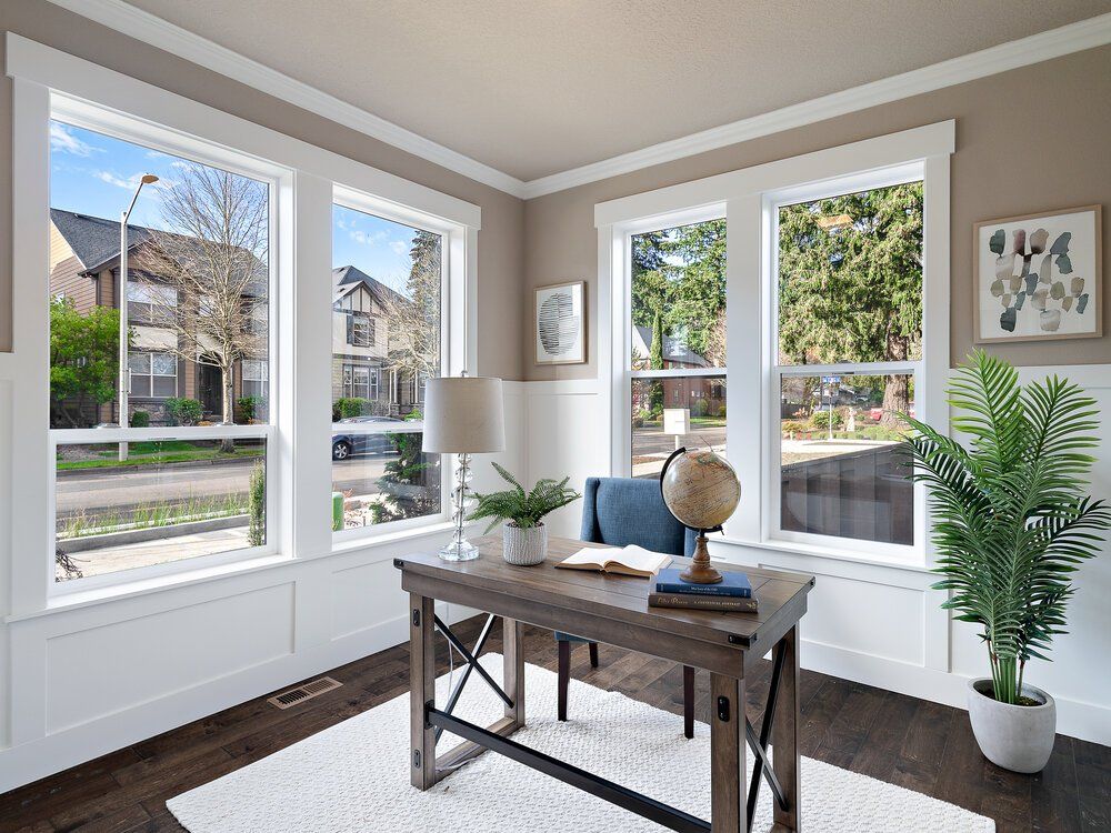 Picture of a desk in corner of room with windows.
