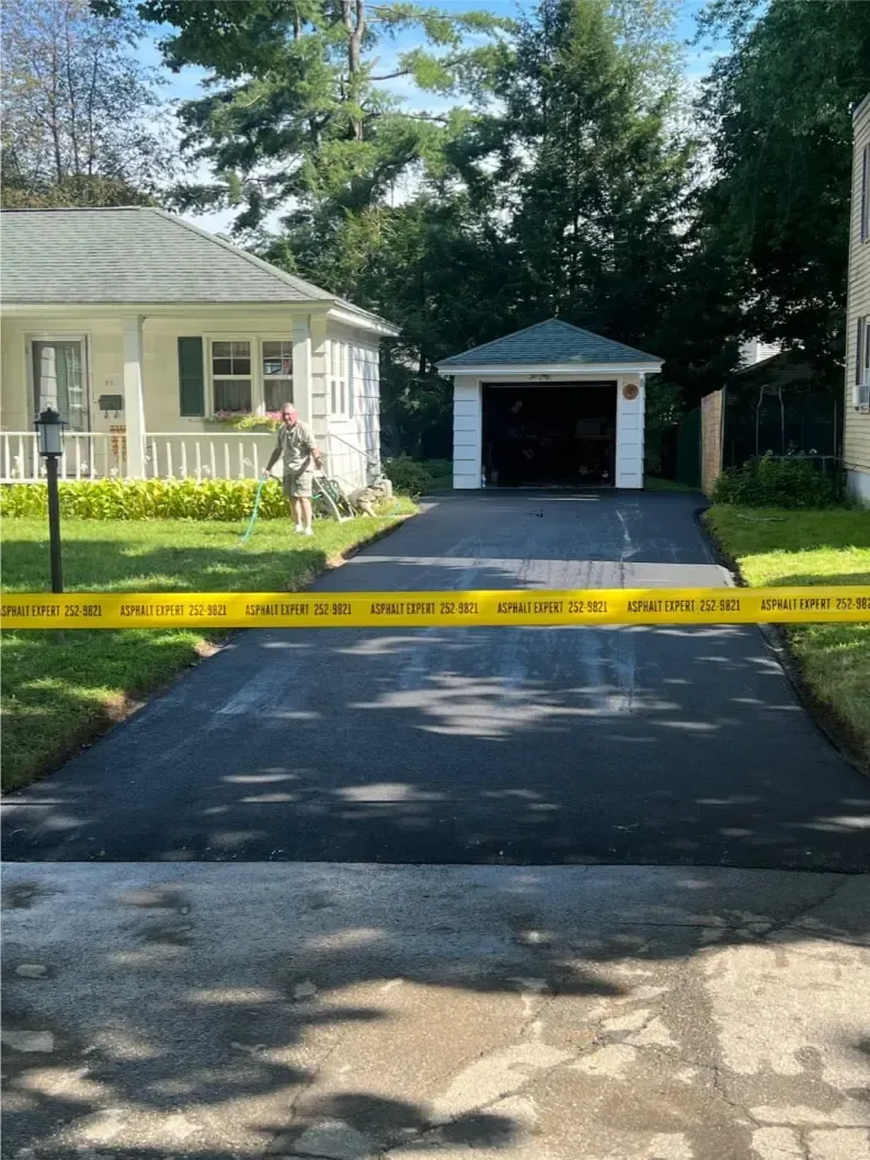 Freshly paved asphalt driveway with yellow caution tape, leading to a garage. 