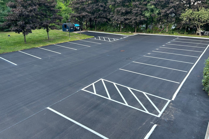 Newly paved parking lot with white painted lines for parking spaces and a crosshatched area.