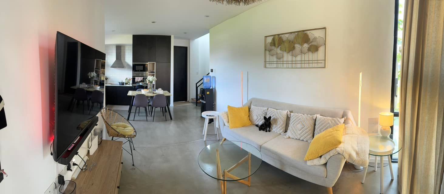 Living room with a sofa, TV, and dining area. A black cat sits on the sofa.