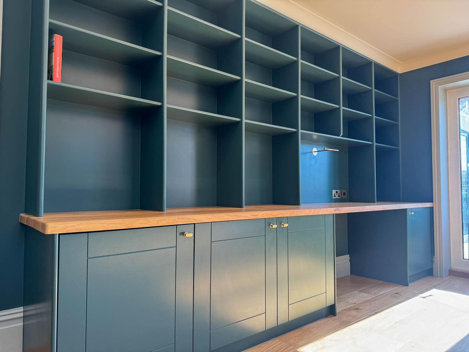 Built-in dark teal bookcase with wooden desk, cabinets, and shelves. Red book on a top shelf.