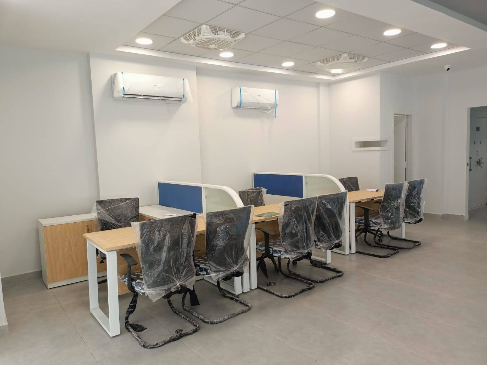 An office space with desks, chairs, air conditioners on white walls.