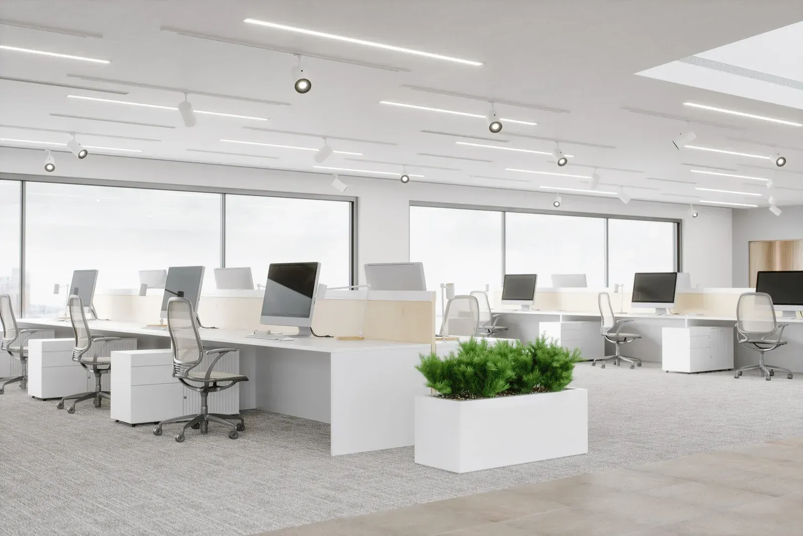 Bright, modern office space with white desks, chairs, and walls. Large windows, plants, and overhead lighting.