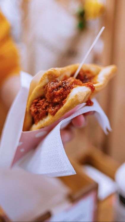 Una mano regge un fagottino di pasta fritta ripieno di ragù di carne rossa, avvolto in un tovagliolo di carta.