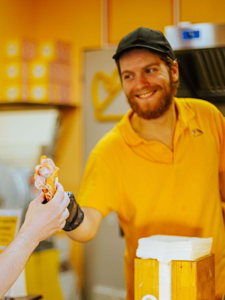 Un dipendente sorridente, con indosso una polo e un berretto gialli, porge un prodotto alimentare confezionato 