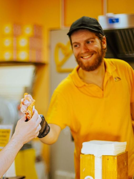 Un dipendente sorridente, con indosso una polo e un berretto gialli, porge un prodotto alimentare confezionato 