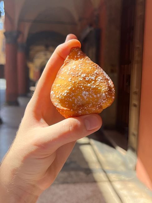 Una mano regge un dolce fritto dorato e cosparso di zucchero a velo