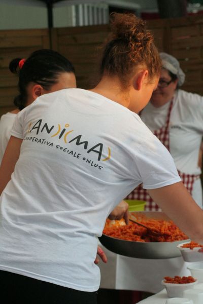 Durante un evento gastronomico, una persona che indossa una maglietta della cooperativa Anima serve della pasta
