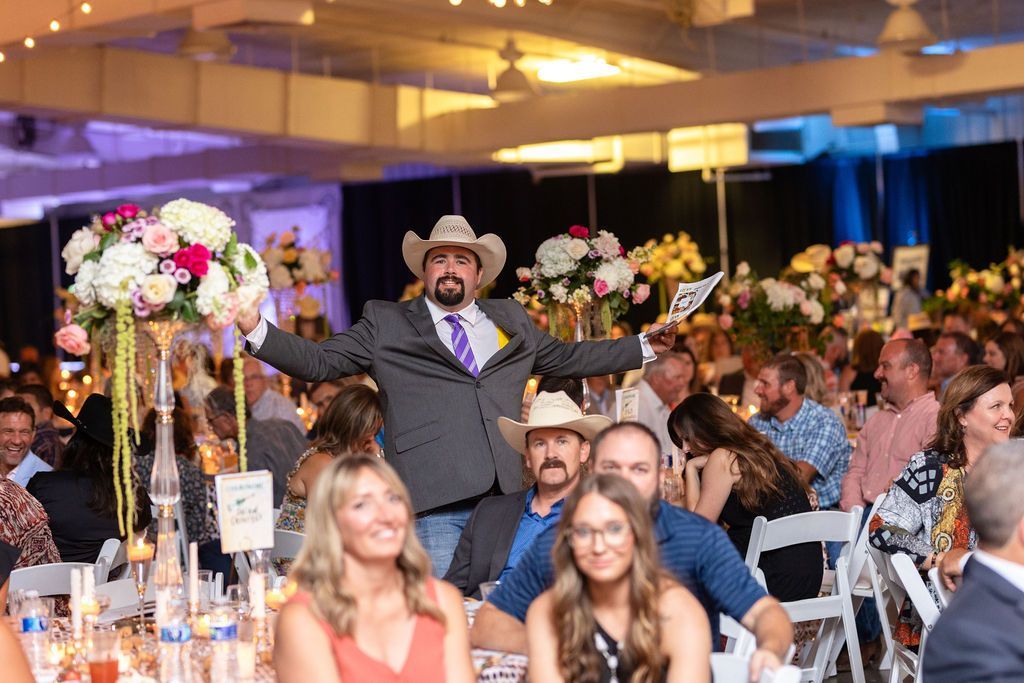 a man in a cowboy hat is standing in front of a crowd of people at a an event 