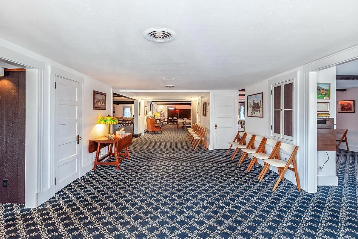Hallway with patterned carpet, white doors and trim, and chairs along the right wall, leading to a furnished room.