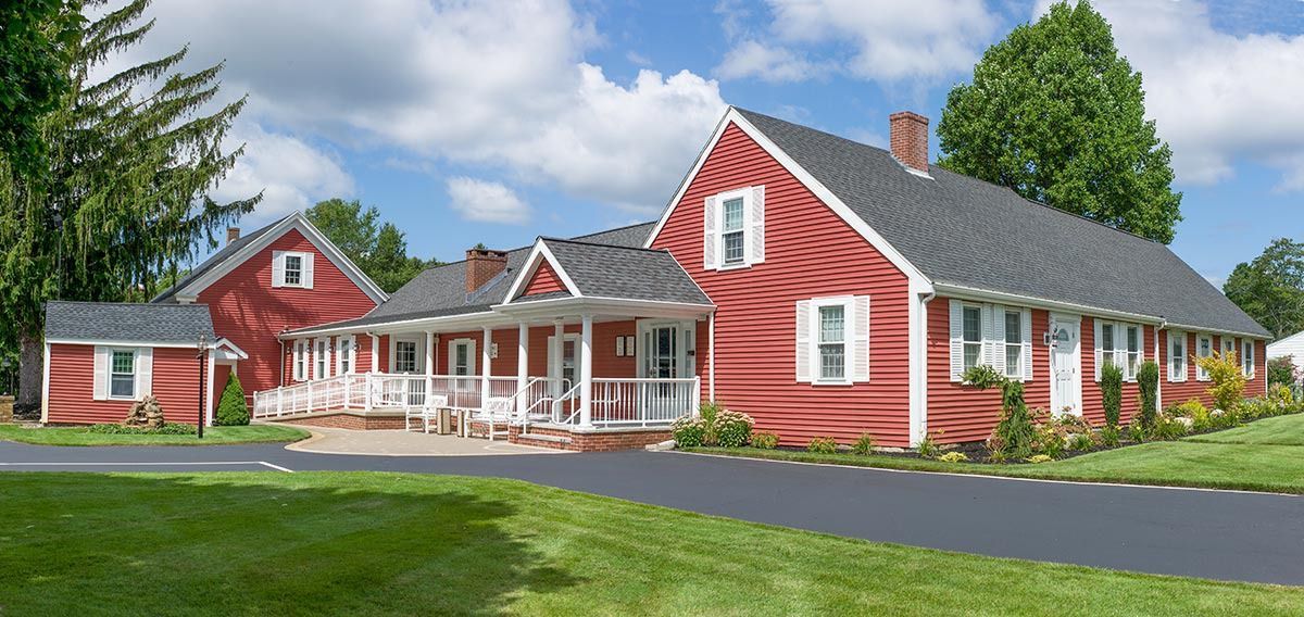 Red house with white trim, porch, and dark gray roof, surrounded by green grass and trees.