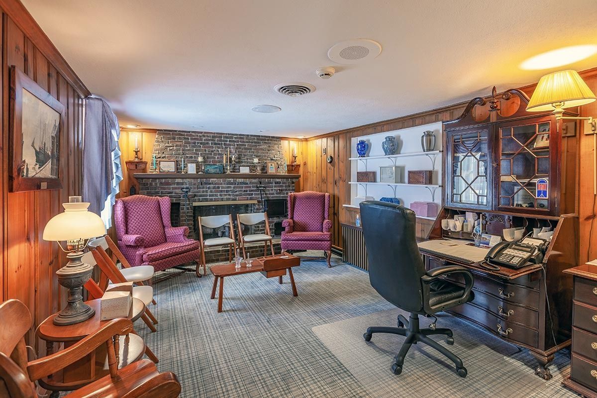 Cozy office with wood paneling, fireplace, armchairs, desk, and lamps.