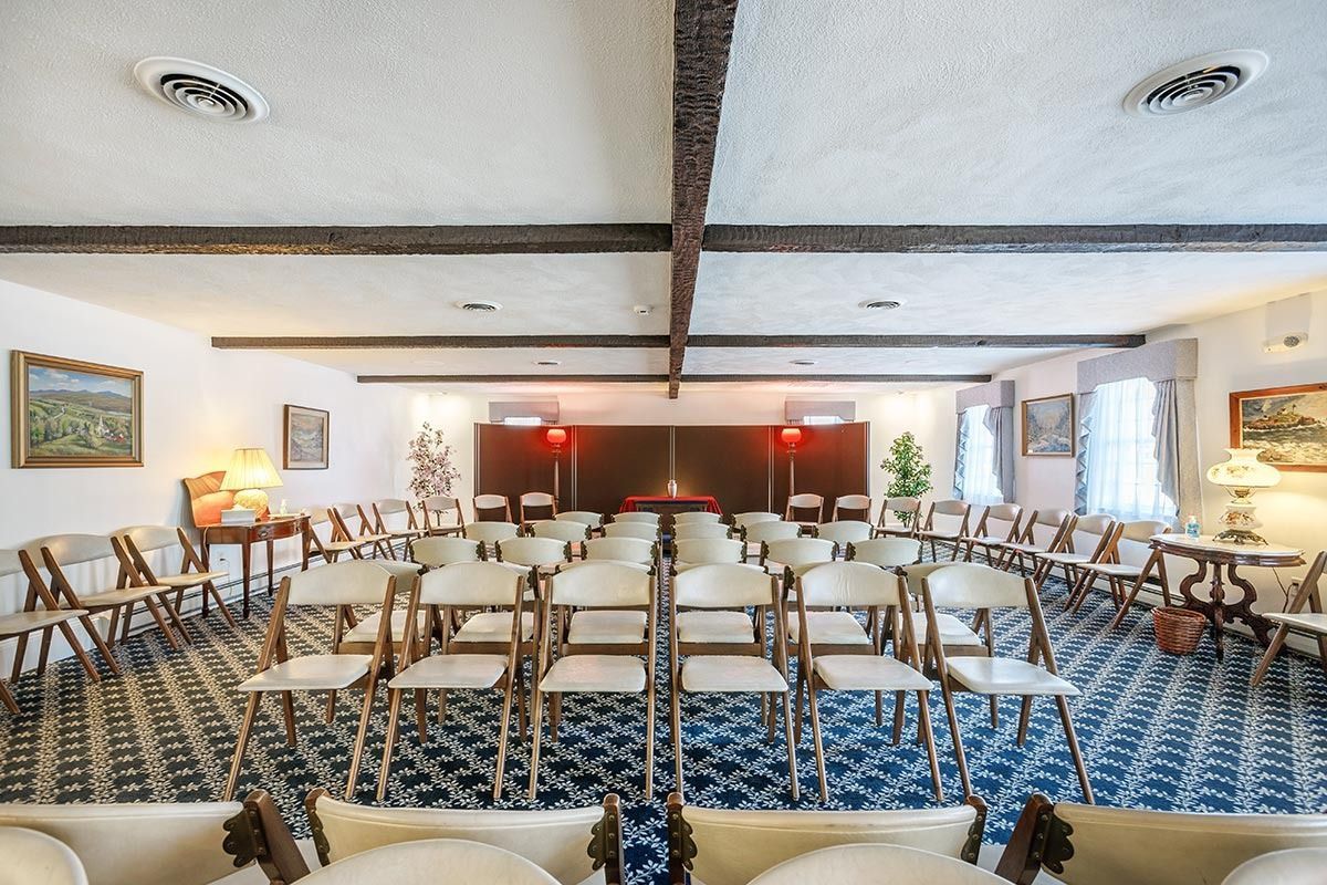 Rows of chairs face a central area in a room with dark wood beams, blue patterned carpet.