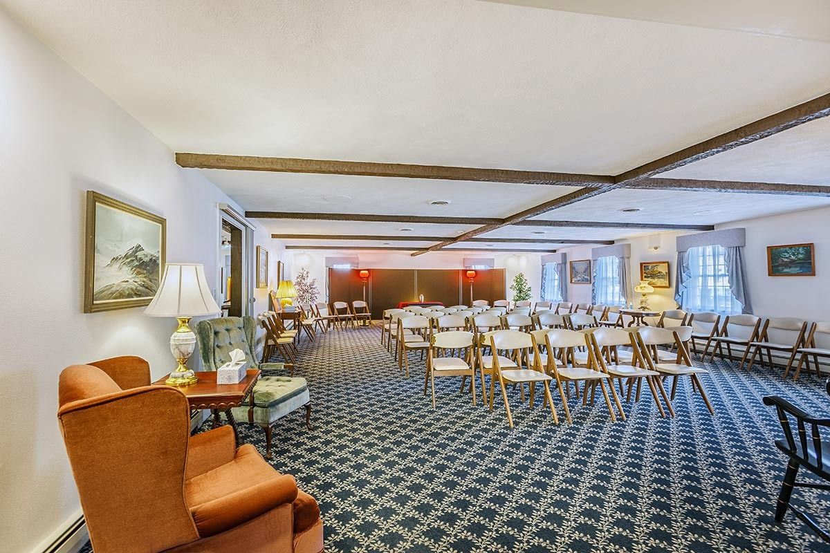 A room with rows of chairs, used for a gathering or ceremony. Antique furniture and art are present.