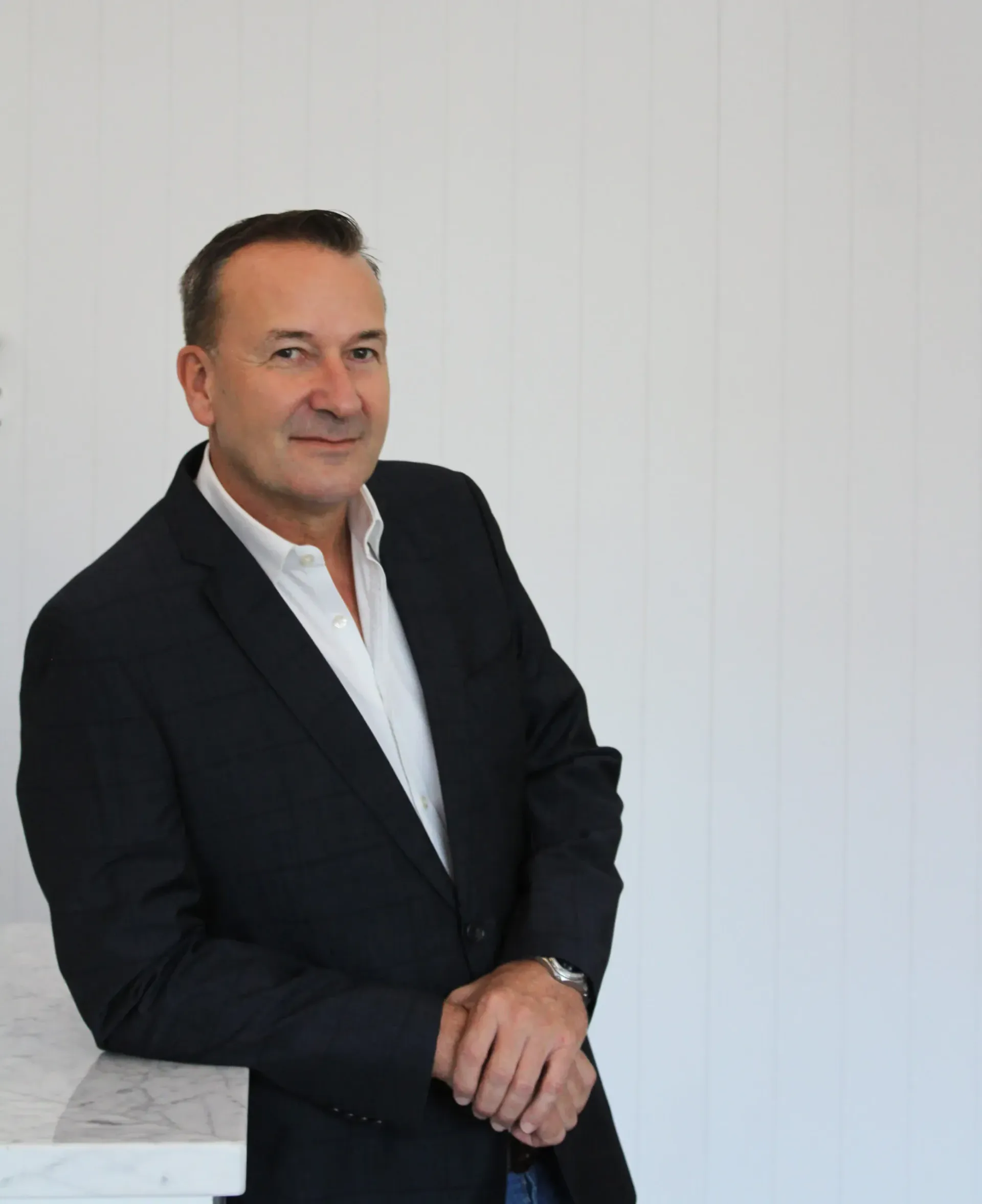A man in a suit is leaning against a white wall