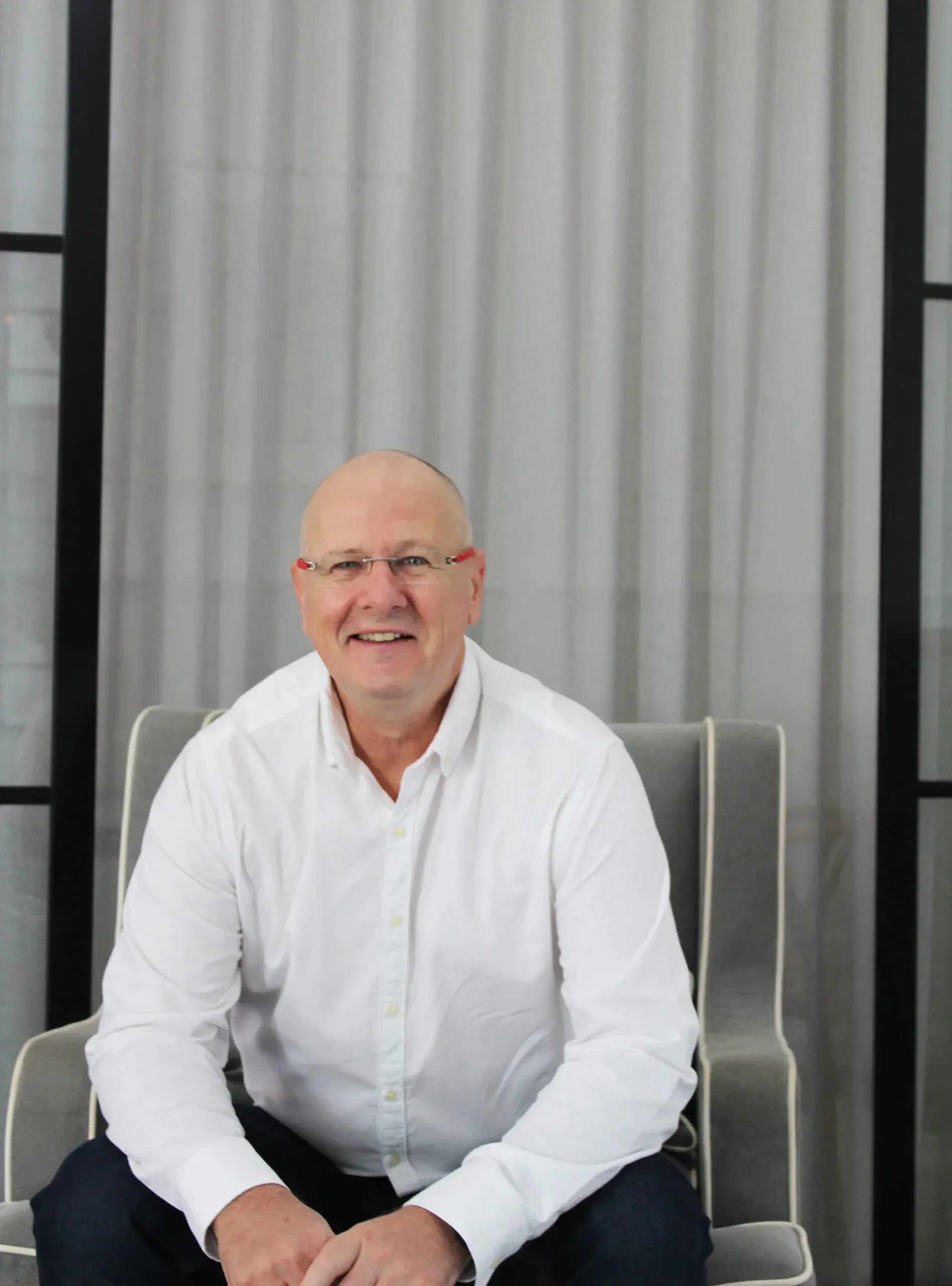 A man in a white shirt is sitting in a chair and smiling
