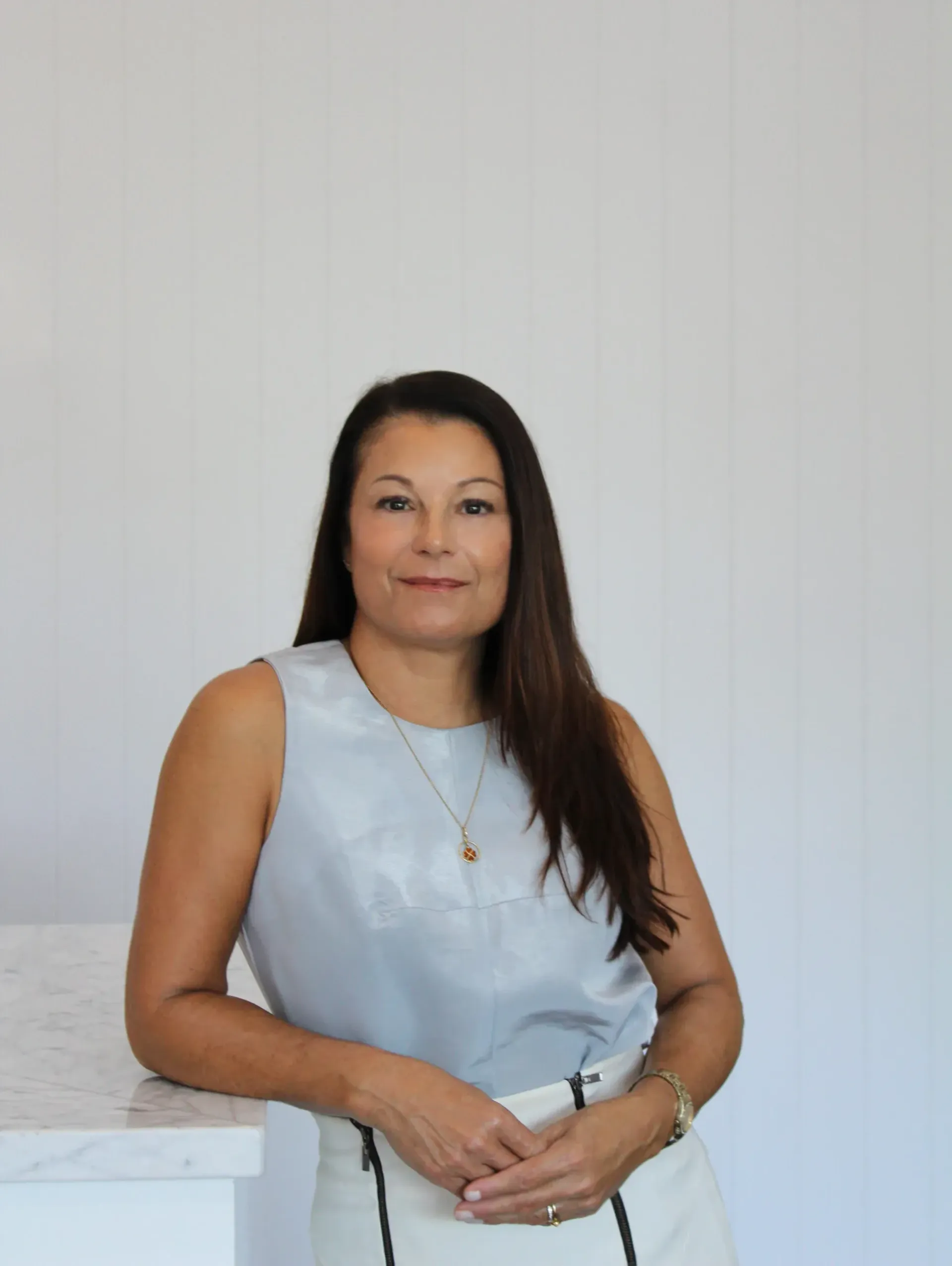 A woman in a blue tank top and white skirt is leaning on a counter.