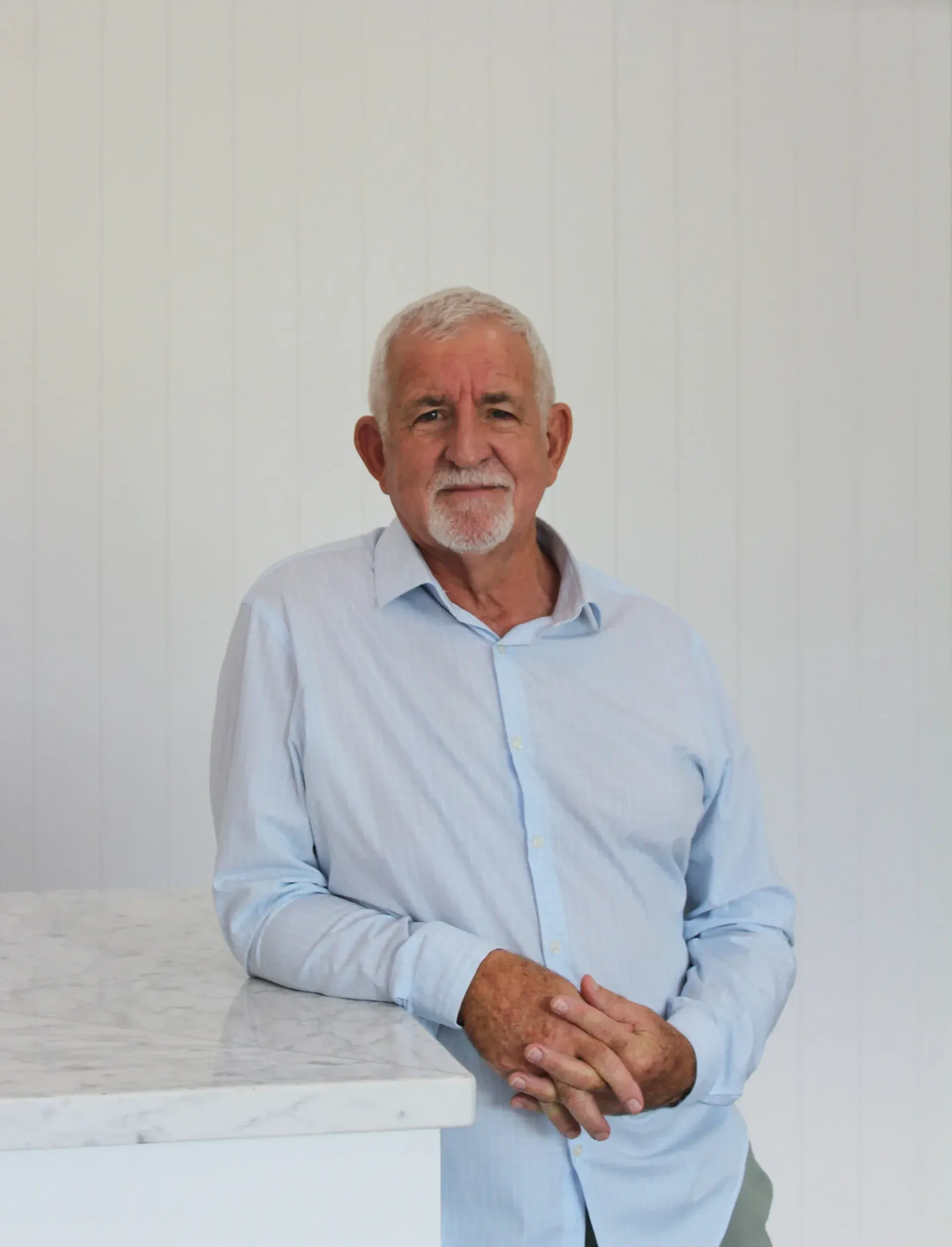 A man with a beard is leaning against a counter with his hands folded.