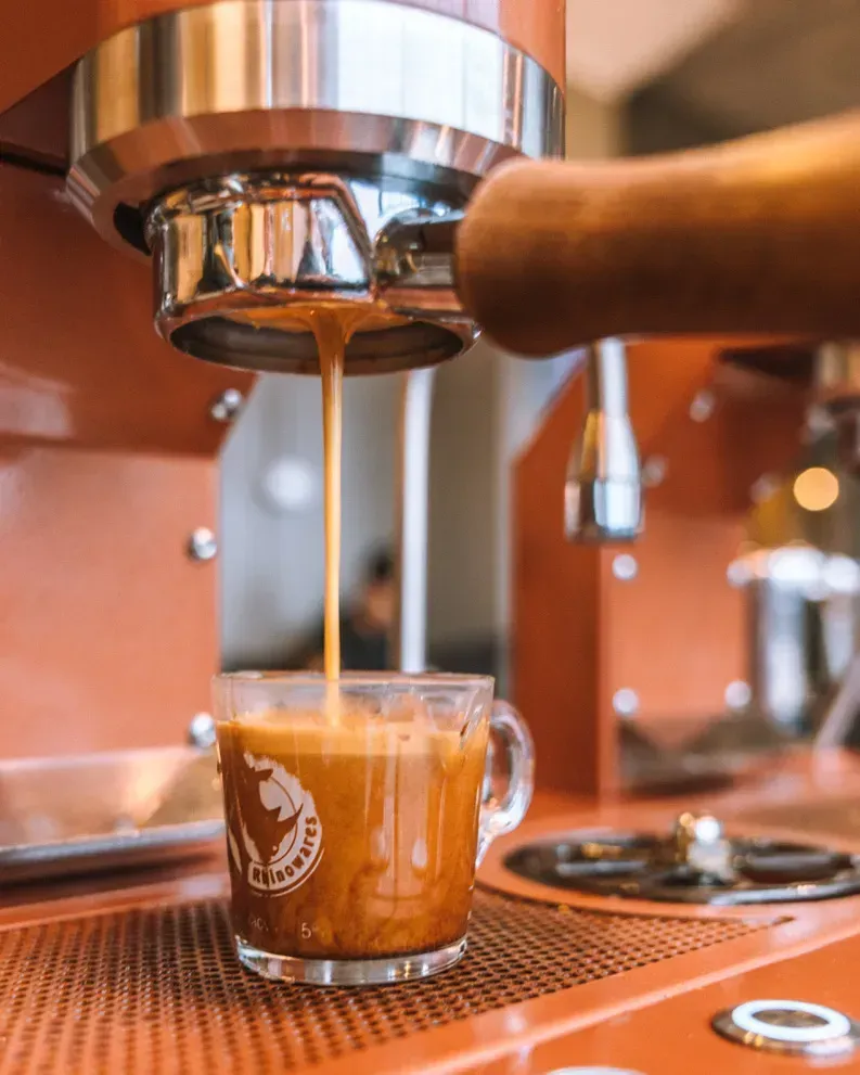 A cup of coffee is being poured into a glass from a coffee machine.