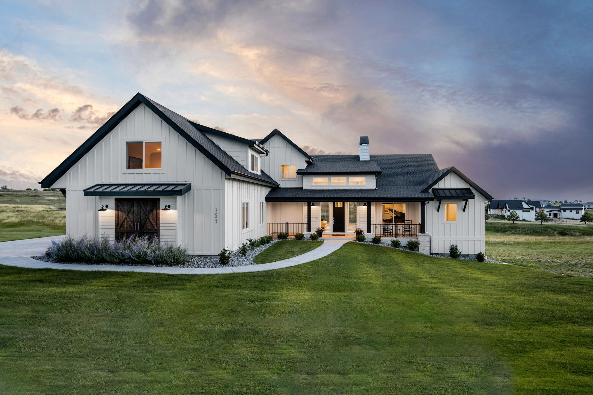 A large white house with a black roof is sitting on top of a lush green field.