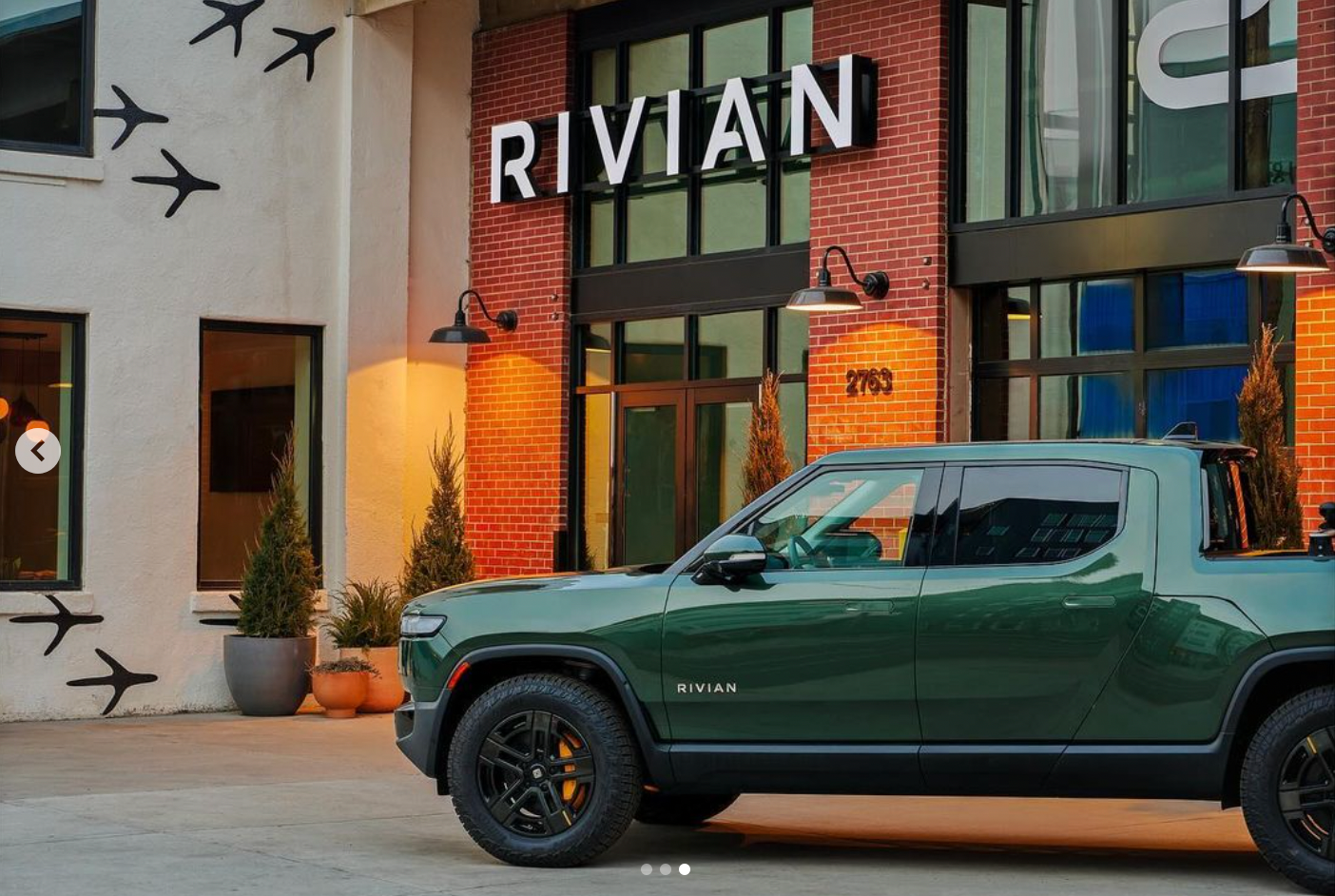 A green truck is parked in front of a building that says rivian.