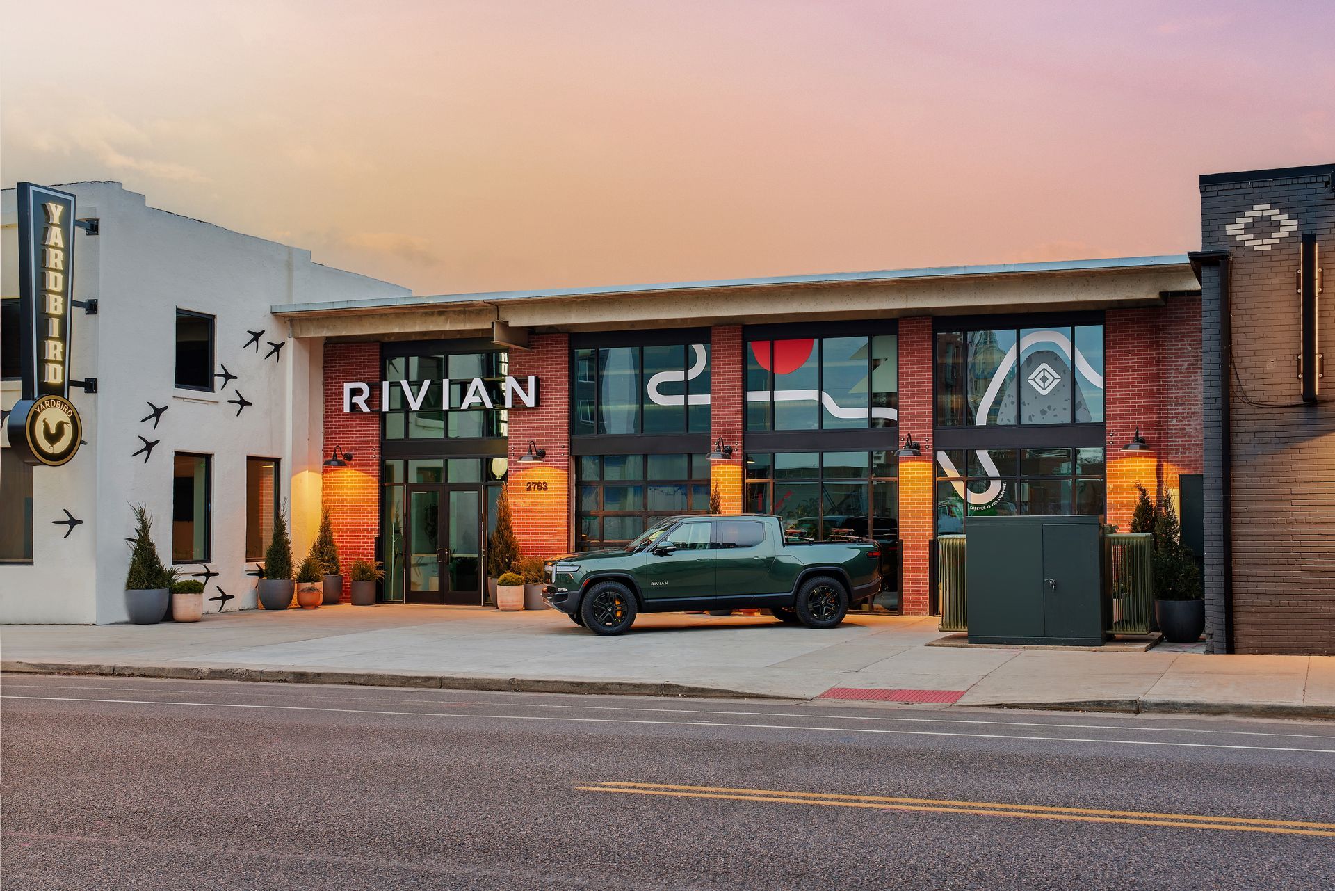 A green Rivian truck is parked in front of a building.