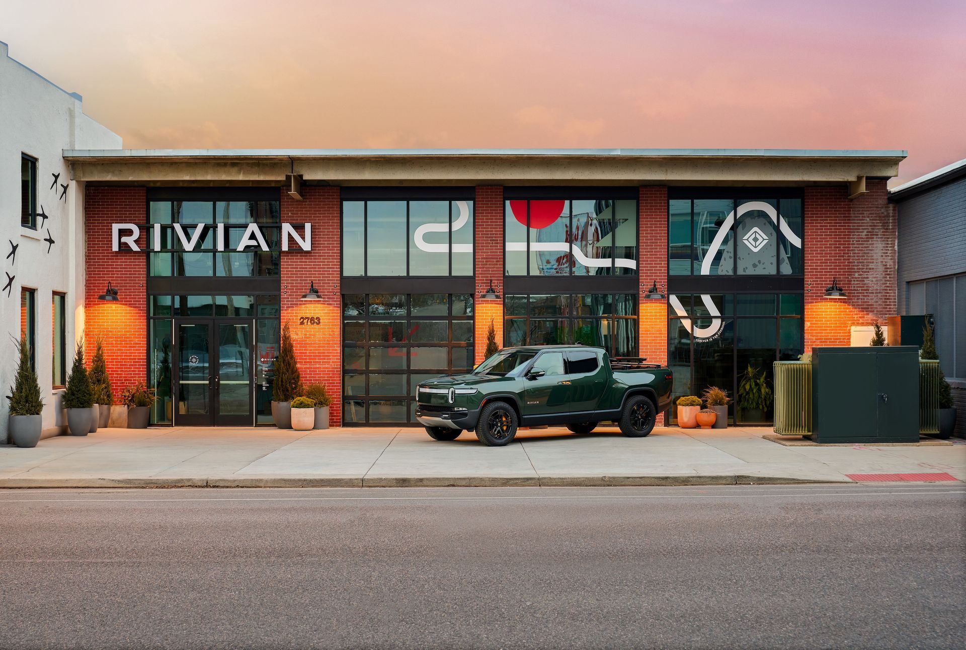 A green rivian truck is parked in front of a building.