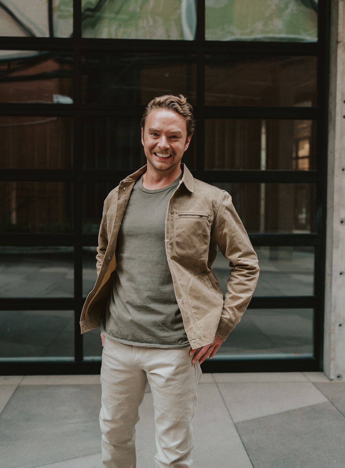 A man is standing in front of a building with his hands on his hips.