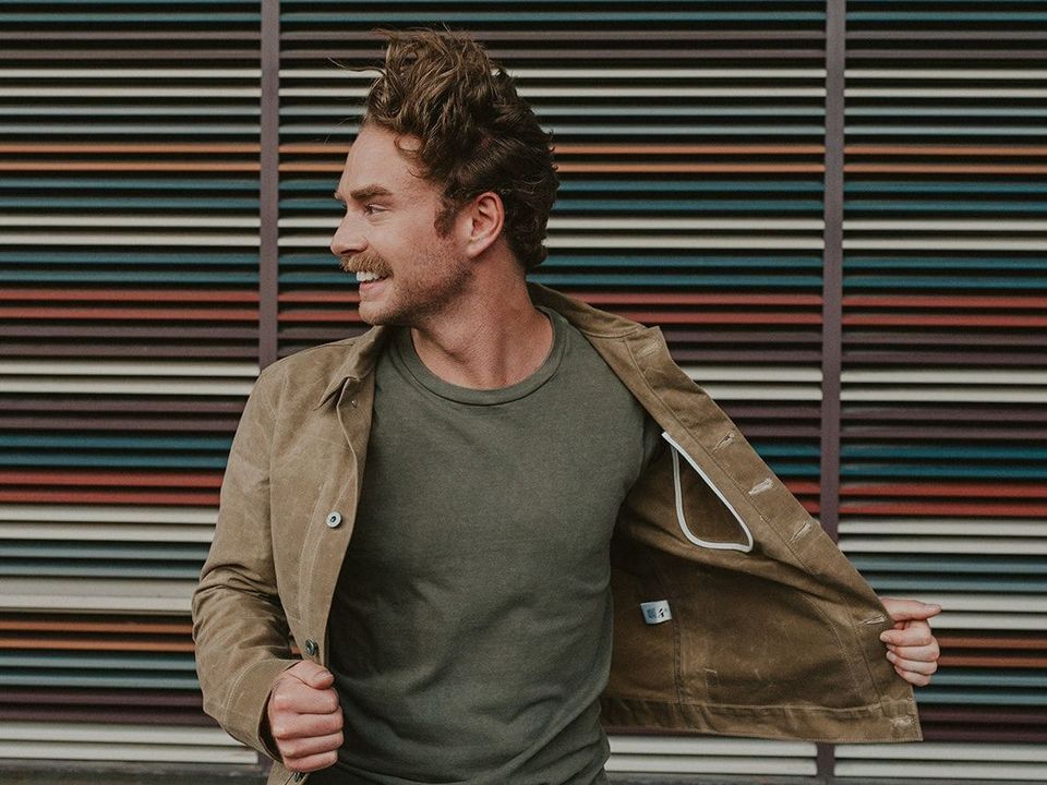 A man is standing in front of a wall with his jacket open.