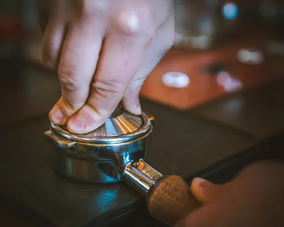 A person is pressing a coffee tamper on a table.