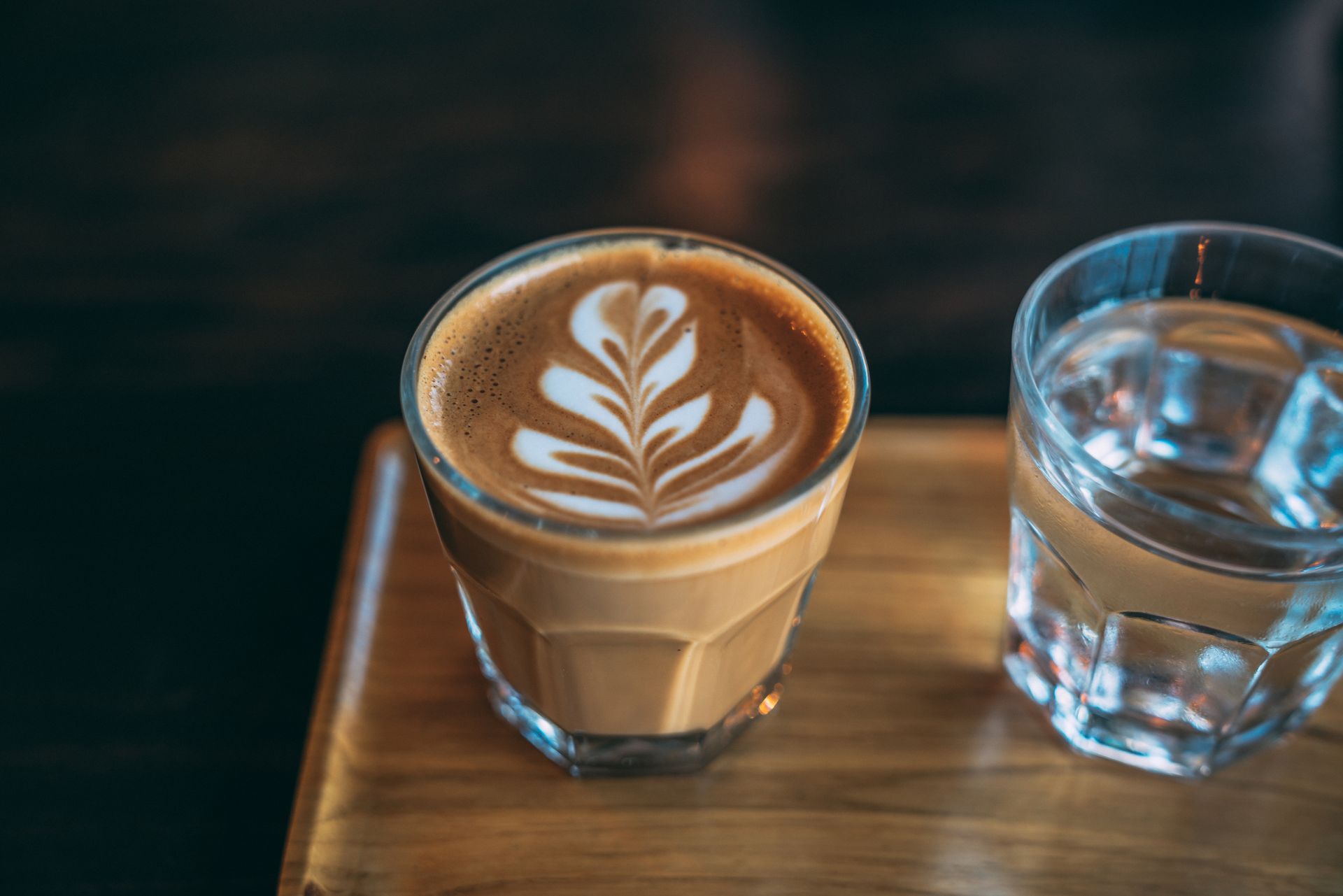 A cup of coffee and a glass of water on a wooden tray.