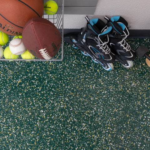 Sports balls and black-and-blue inline skates on a green speckled floor by a wire shelf.