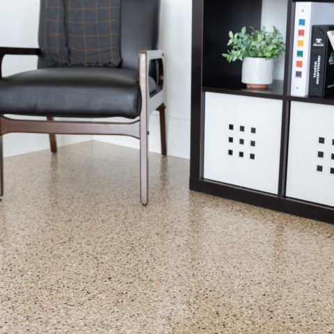 Black chair beside a shelving unit with a potted plant on a speckled floor indoors