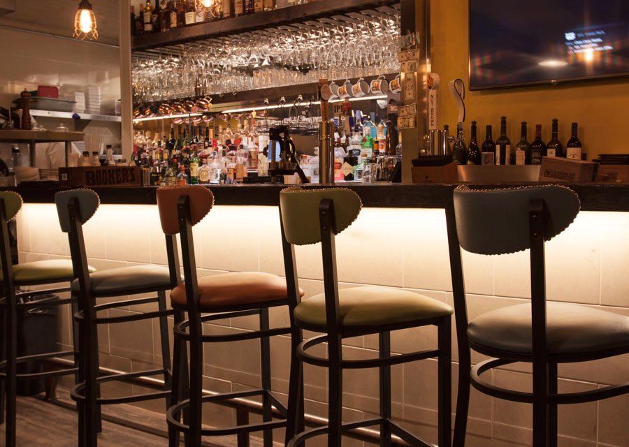 Bar with colorful stools, bottles, and glasses. Bright overhead lighting.
