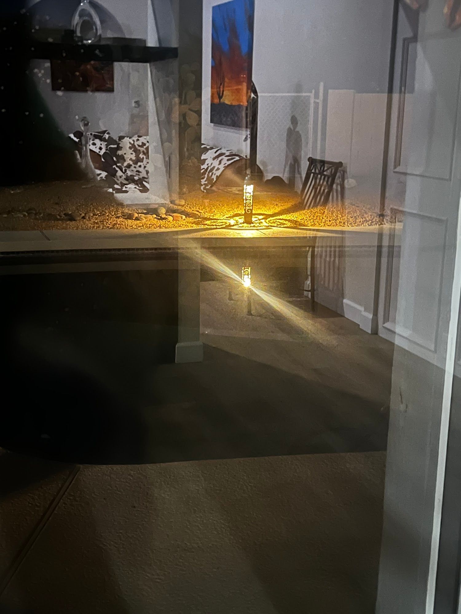 Reflection in glass: room interior with art, a lit candle, and a dark rug.