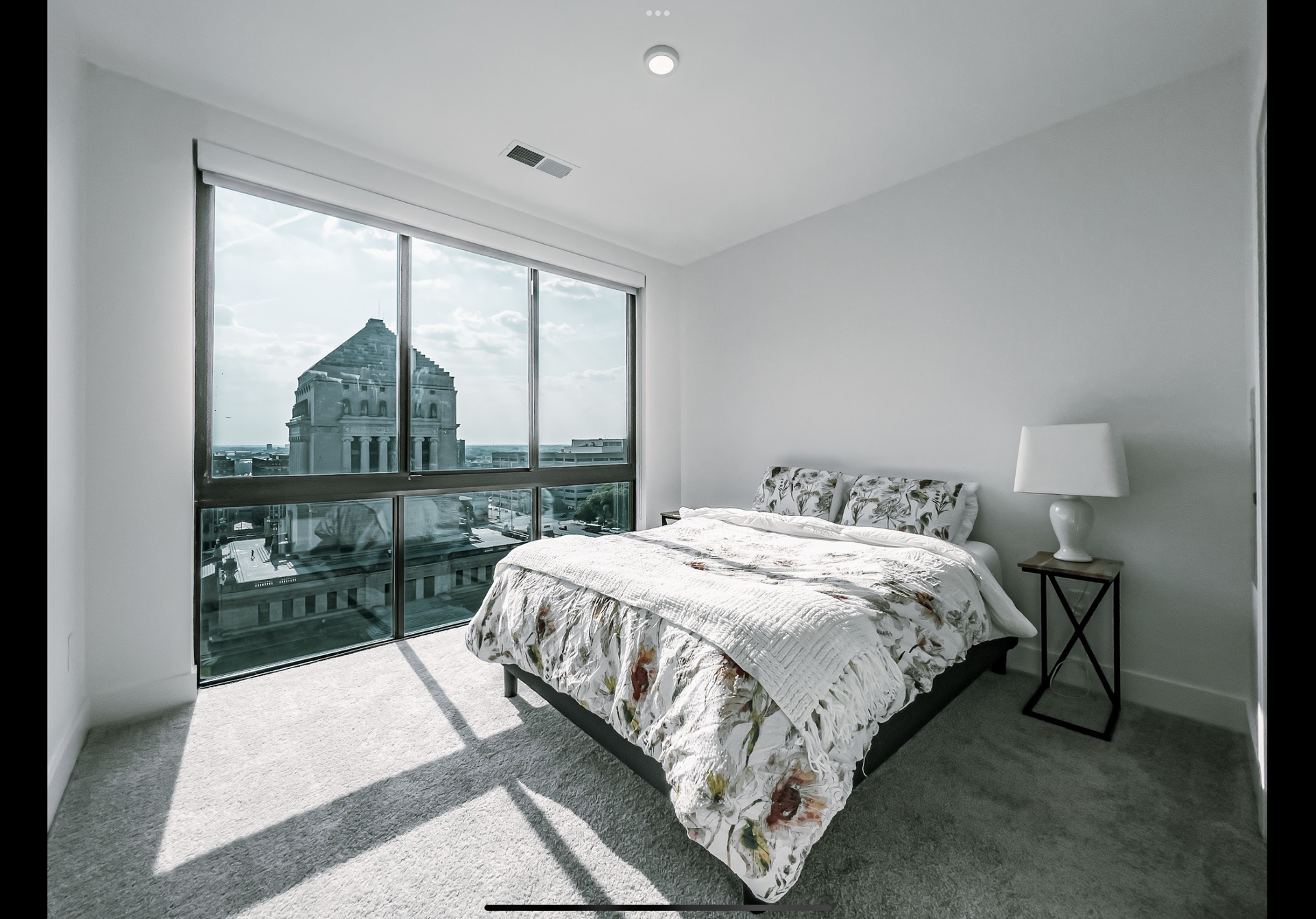 Modern bedroom with a white floral comforter and a large window offering a view of an ornate stone building.
